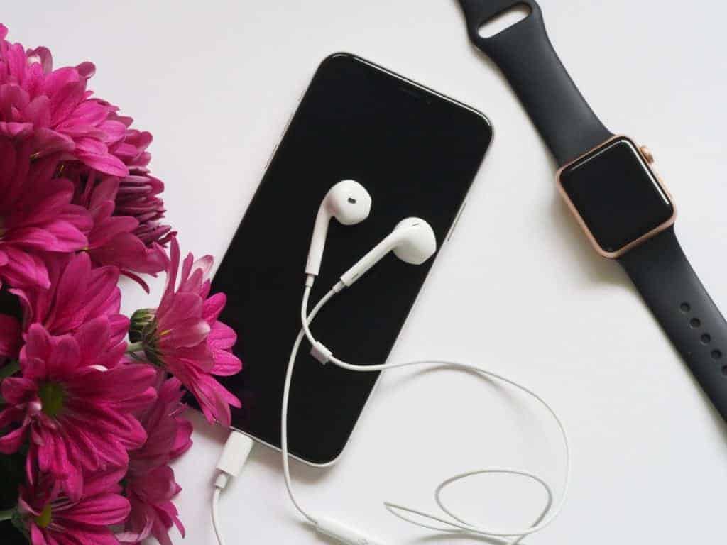 cell phone on table with headphones and pink flowers