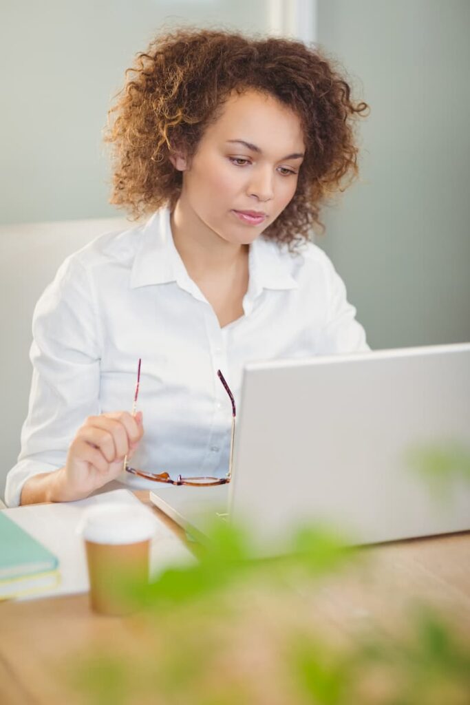 a woman in front of her laptop holding her eyeglasses and like to sell digital downloads on etsy