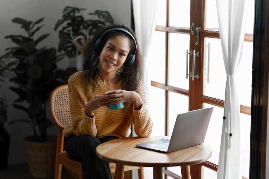 a woman holding a cup in front of a laptop searching for the best transcription jobs from home with no experience