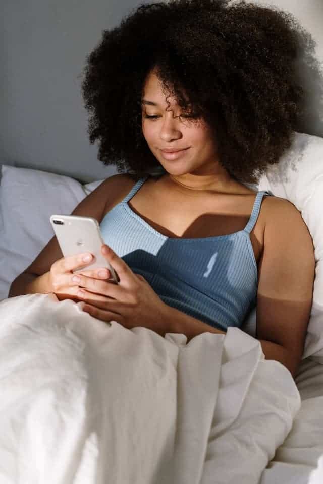 a woman lying on her bed while using her phone to redeem the $750 Shein gift card