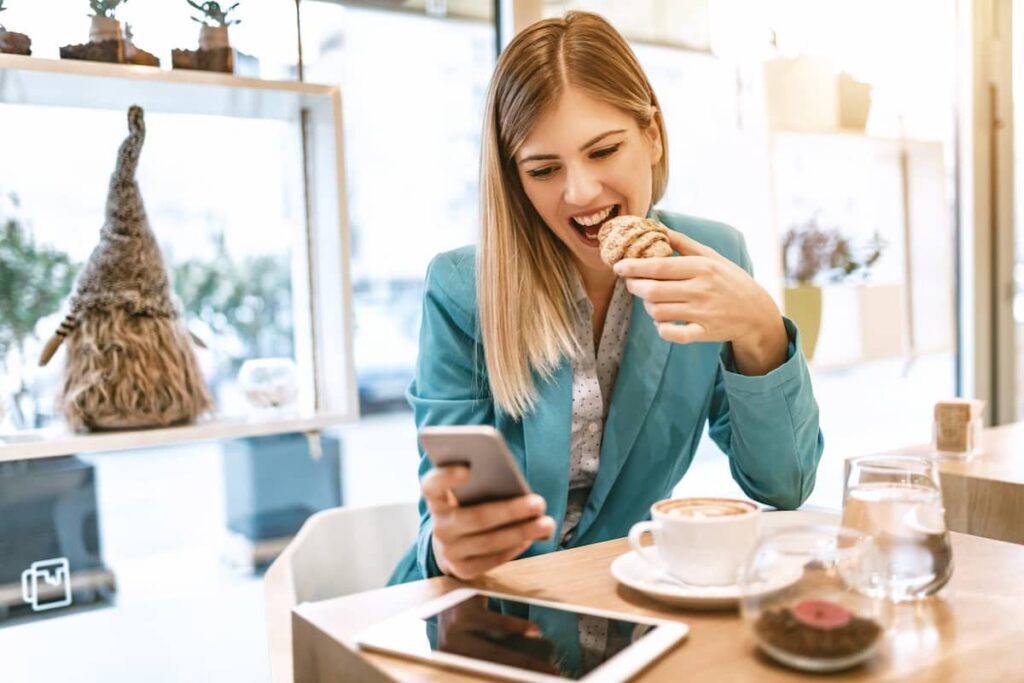a woman eating a bread and using her phone