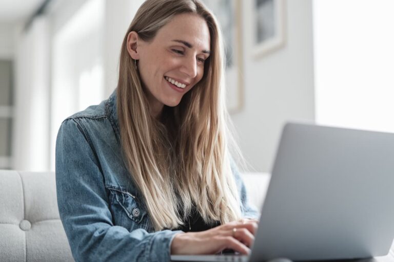 woman smiling as she uses a laptop to create digital products that sell well