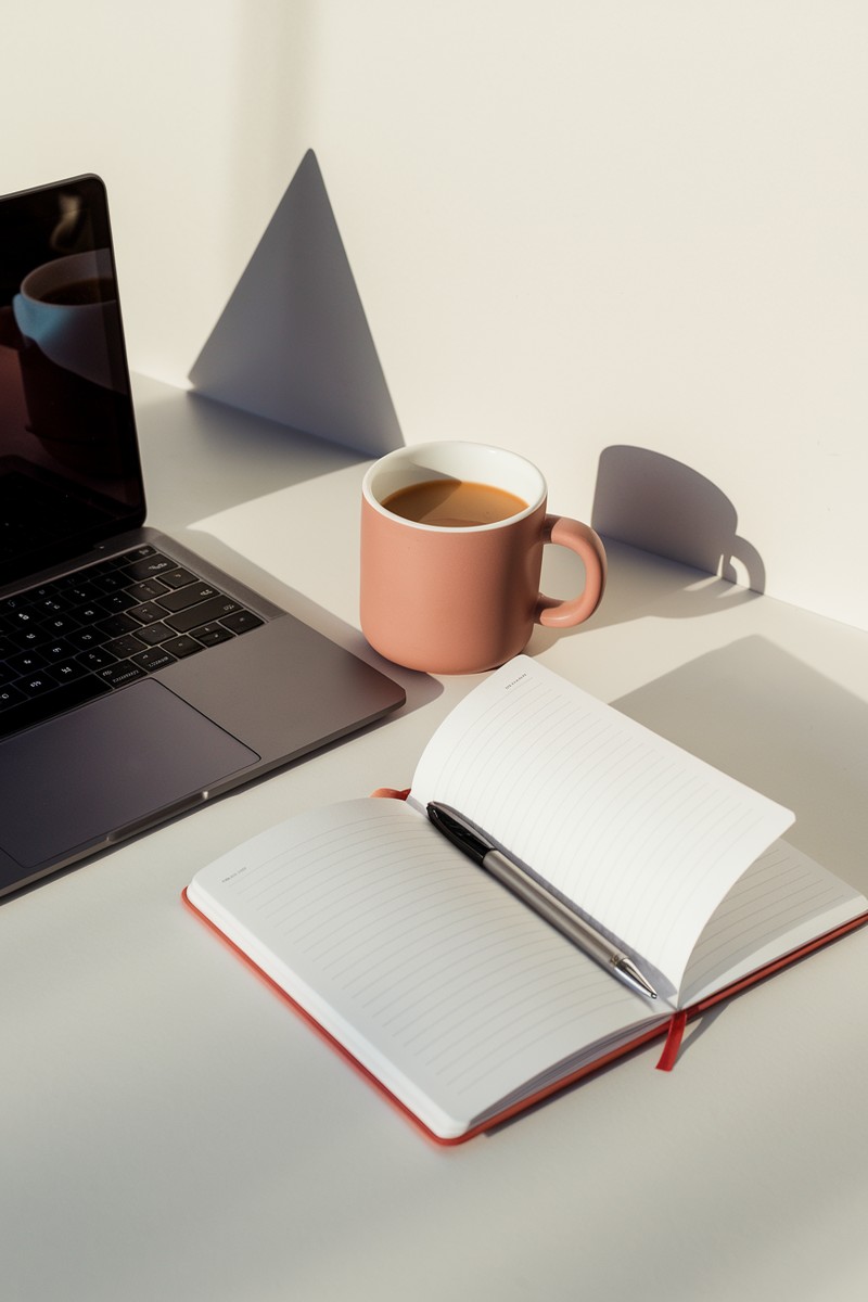 flatlay of laptop, coffee mug, notebook, and pen