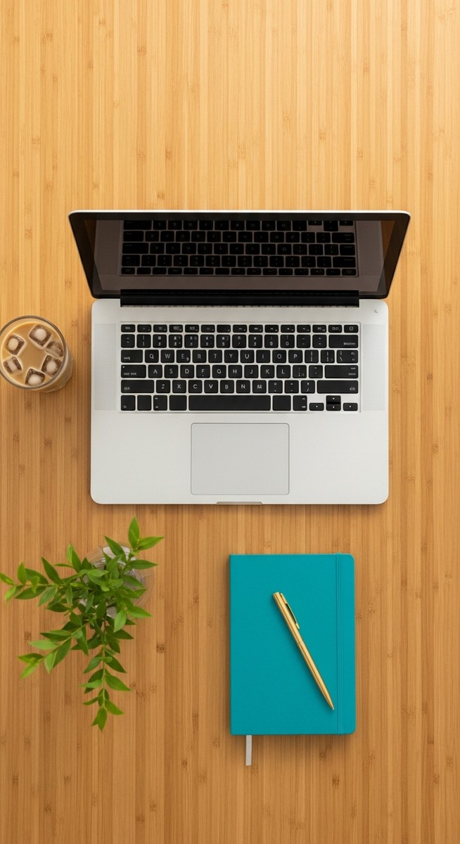flatlay of a laptop and teal notebook on a wooden desk