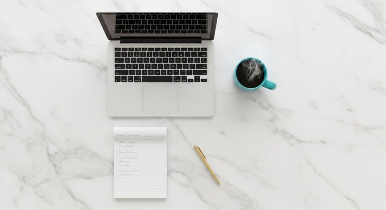 flatlay of a laptop and teal mug on a marble surface