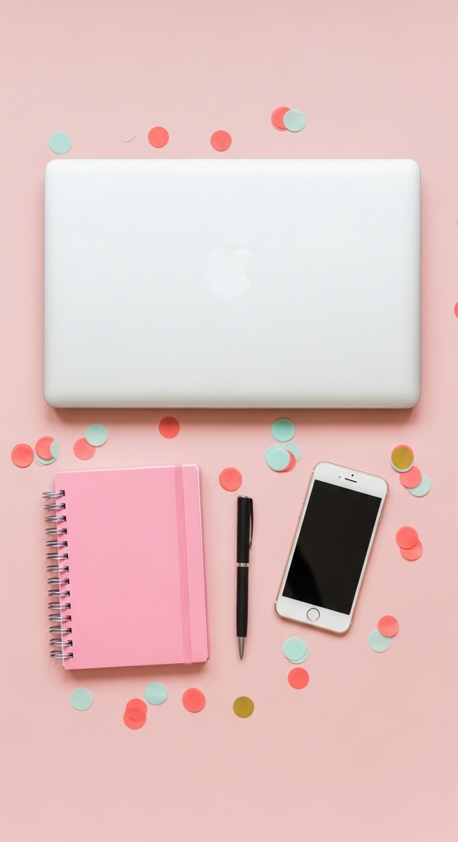 a pink flatlay with laptop, notebook, and phone for budgeting