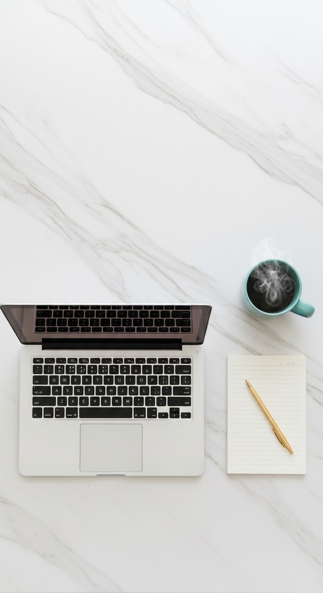 flatlay of a laptop and teal mug on a marble surface