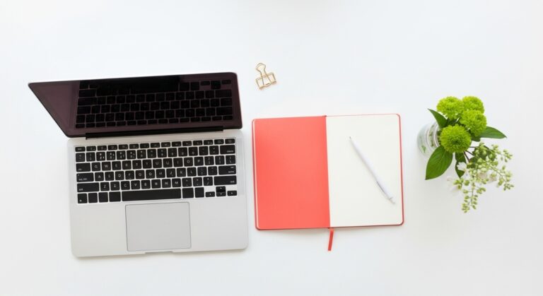 a flatlay with laptop and other items on a white surface for saving money