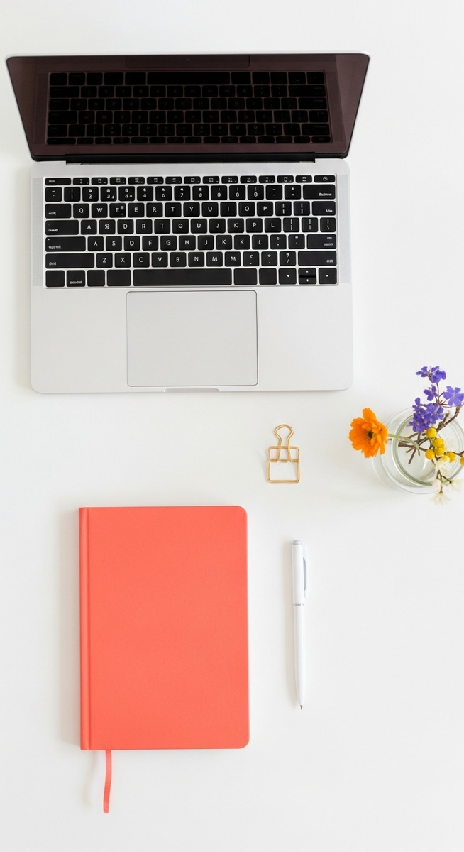a flatlay with laptop and other items on a white surface to live frugally