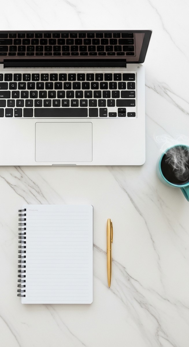 flatlay of a laptop and teal mug on a marble surface