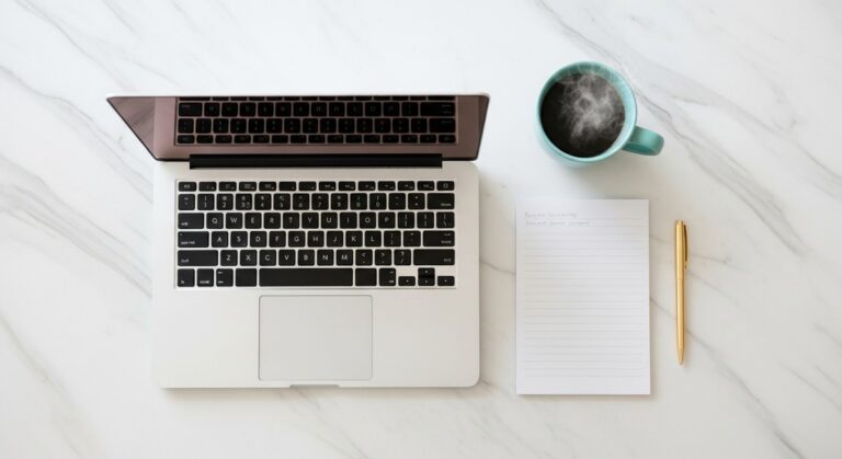 a flatlay of a laptop and teal mug on a marble surface for saving money