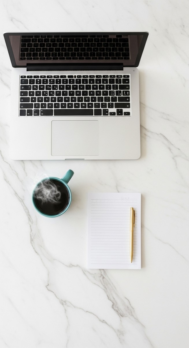 a flatlay of a laptop and teal mug on a marble surface for budgeting