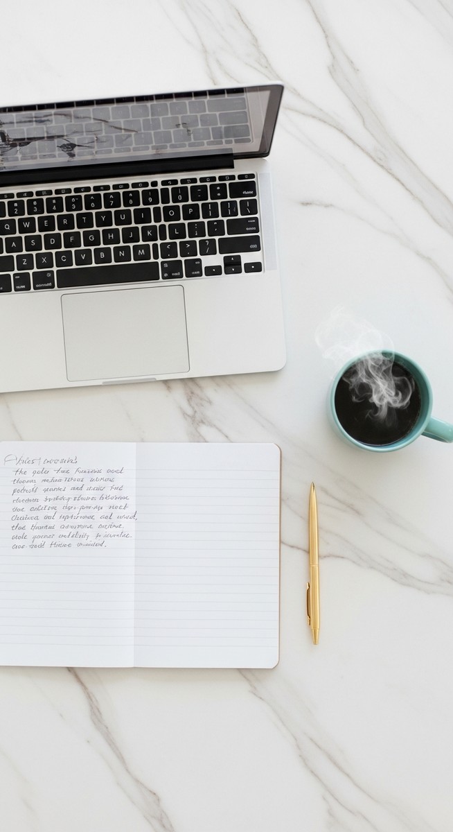 flatlay of a laptop and teal mug on a marble surface