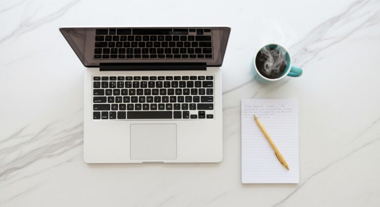a flatlay of a laptop and teal mug on a marble surface to work from home