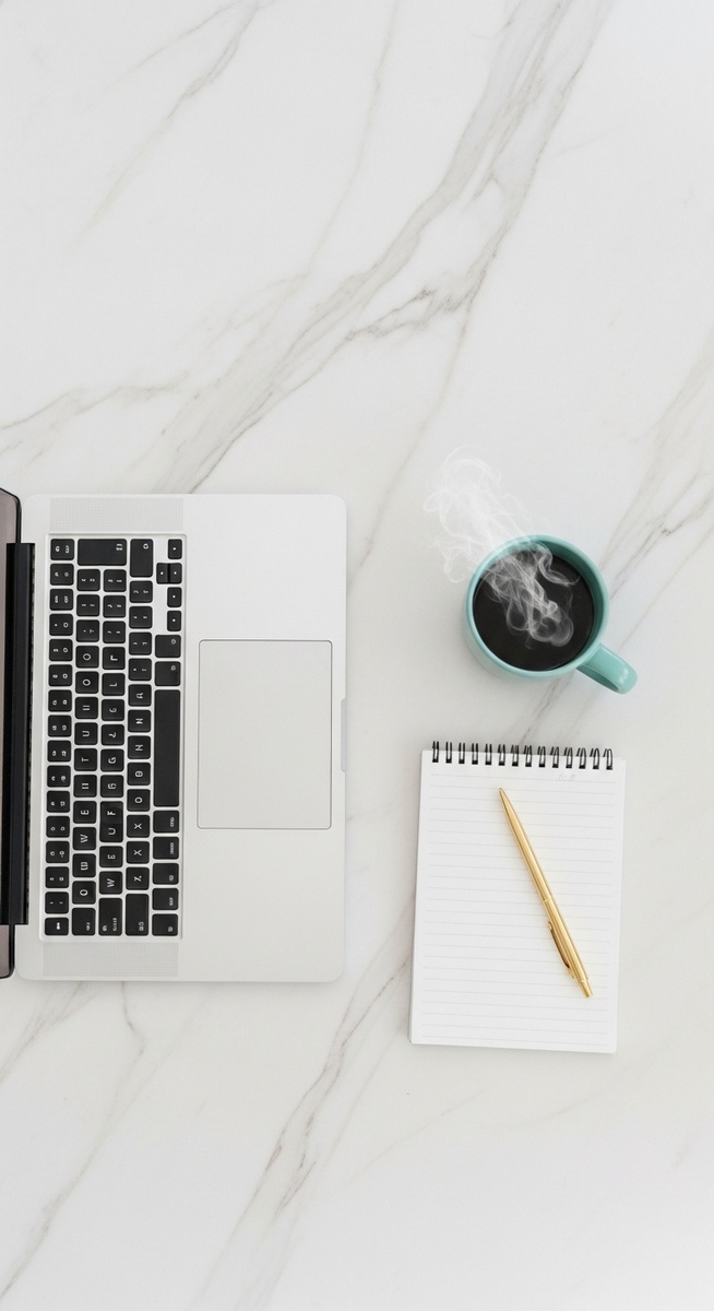 flatlay of a laptop and teal mug on a marble surface